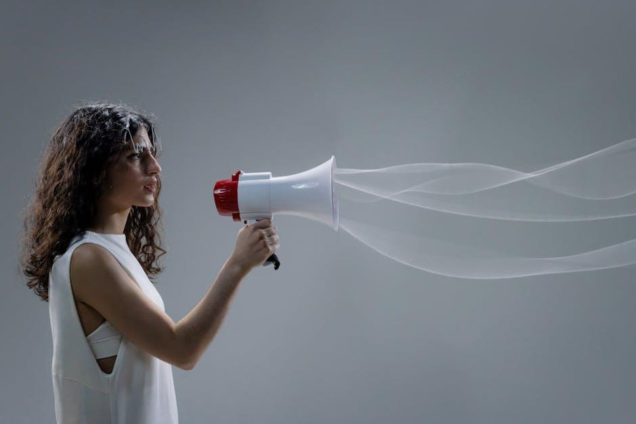 Tecnologia_UltraWave_vibrazioni_uniche_ZDSJFSe5Os - Confidenze24 Source: cottonbro studio - pexels - Woman using a megaphone emitting sound waves on a gray background.
