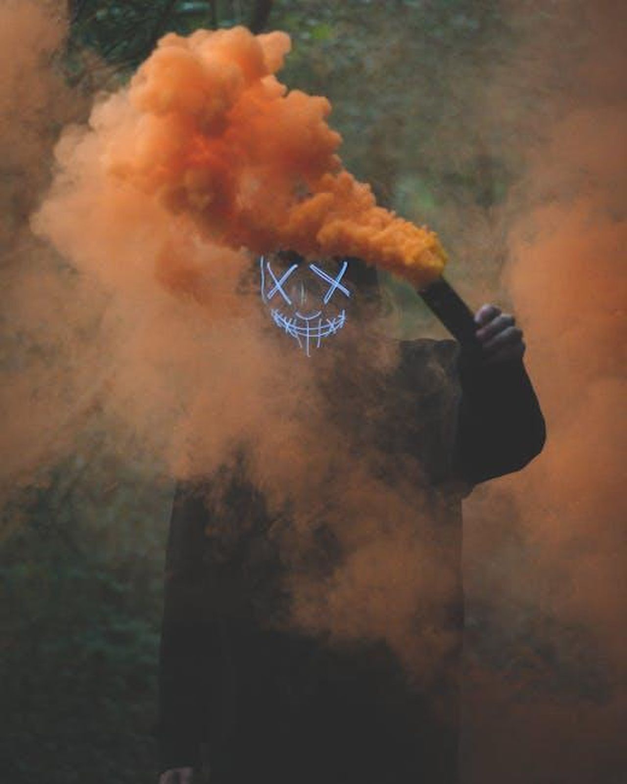Teoria_3_Teddy_ha_ucciso_qualcun_altro_us1AoHbxme - Confidenze24 Source: Connor Danylenko - pexels - A person wearing an LED mask holds a smoke bomb, enveloped in vivid orange smoke.