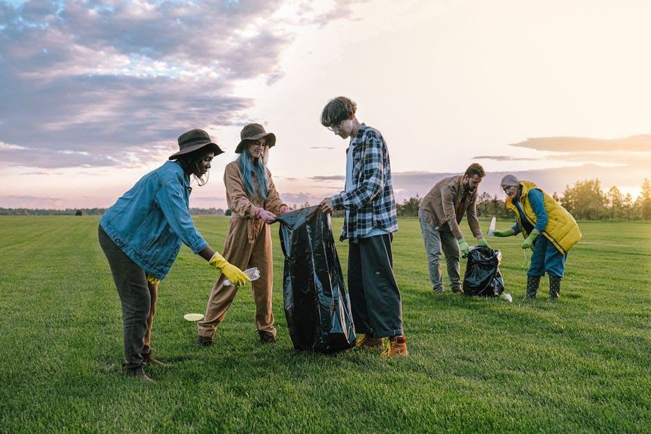 Teorie_sulla_causa_della_morte_wy2SLfNPJU - Confidenze24 Source: Anna Shvets - pexels - A diverse group of volunteers collecting trash in a field at sunset, promoting environmental awareness.
