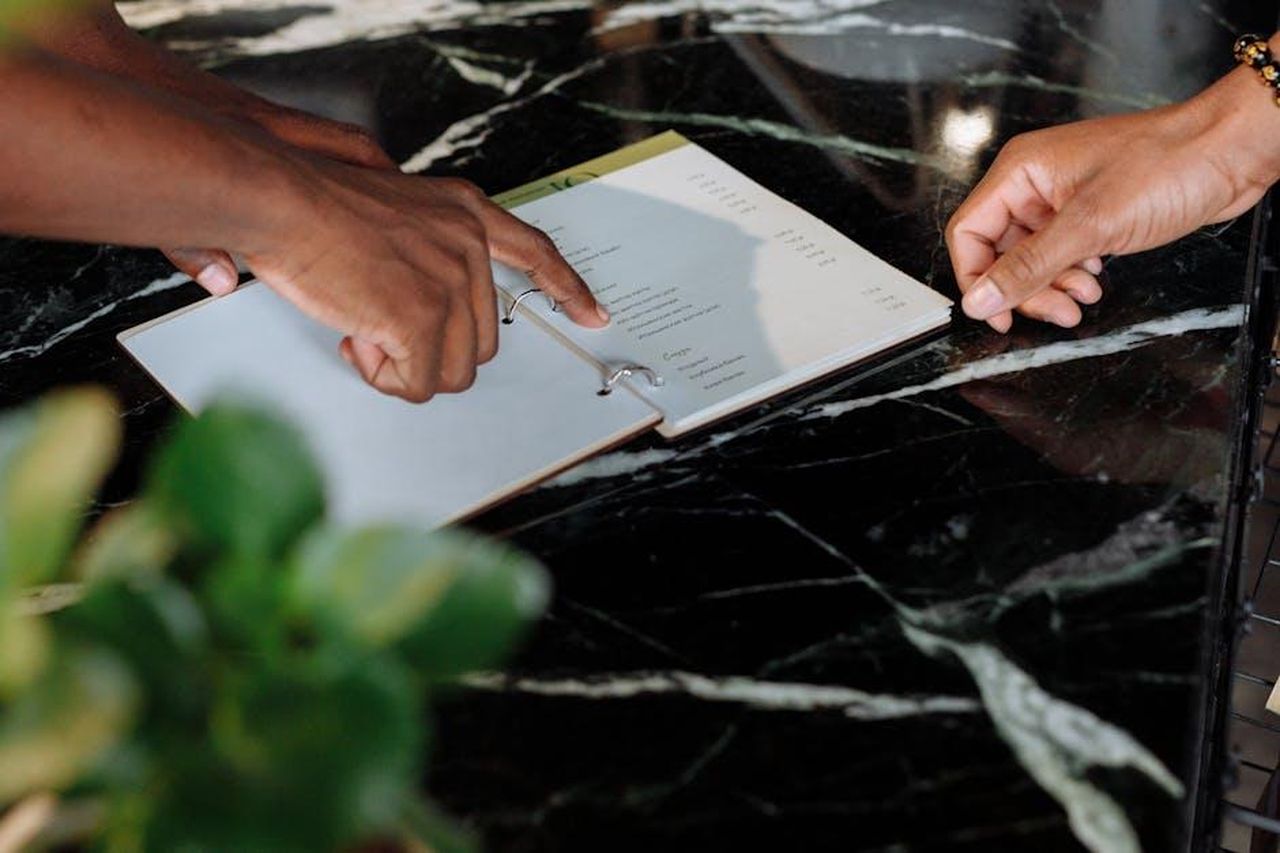 Testimonianze_dei_clienti_soddisfatti_lwVPL0ii6A - Confidenze24 Source: Thirdman - pexels - Hands pointing at menu on black marble counter inside a shop.
