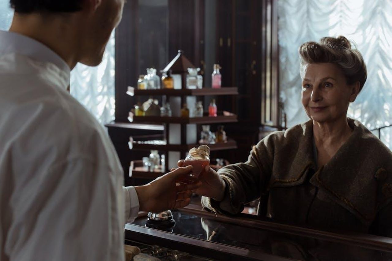 Testimonianze_di_chi_ama_Guerlain_Shalimar_xR3YQPDoqx - Confidenze24 Source: cottonbro studio - pexels - A senior woman receives a perfume bottle from a pharmacist inside a vintage pharmacy.