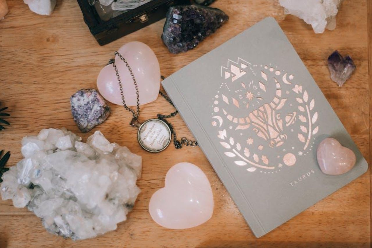 Toro_20_aprile__20_maggio_i7nTrip5IA - Confidenze24 Source: Alina Vilchenko - pexels - Taurus-themed notebook surrounded by heart-shaped and raw crystals on a wooden surface, evoking tranquility.