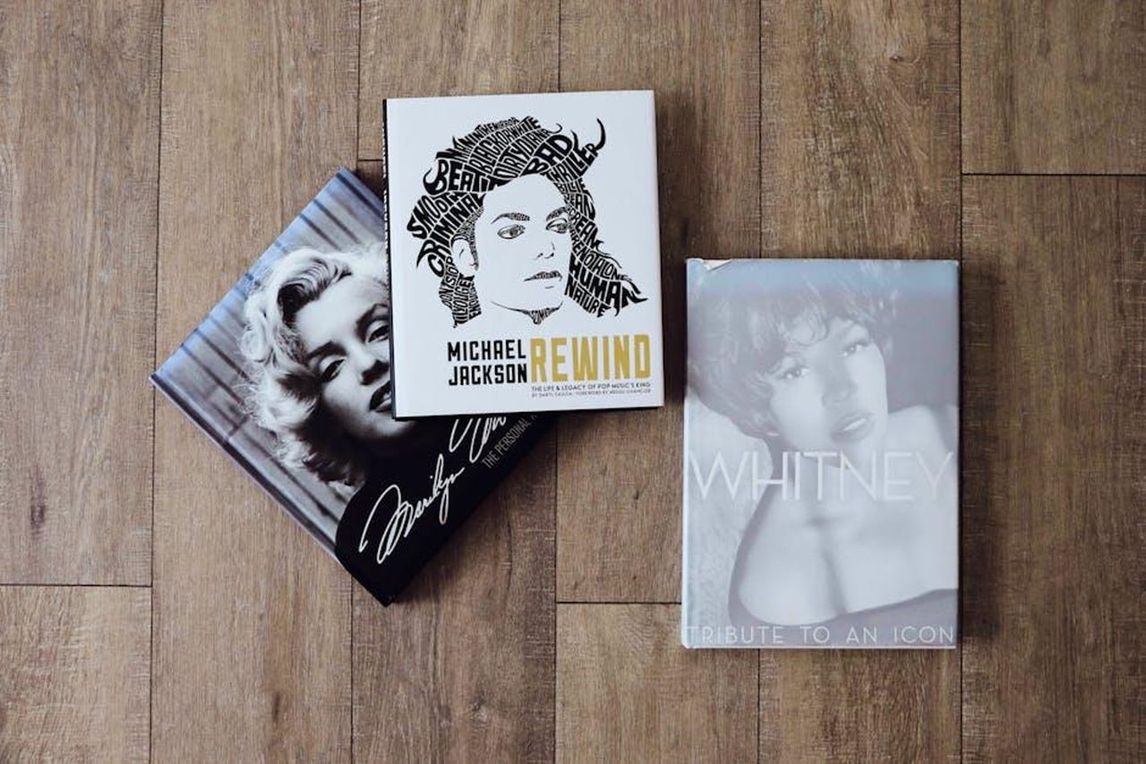 Tributi_delle_Celebrit_AjGwdk1l4s - Confidenze24 Source: Designecologist - pexels - Books featuring Marilyn Monroe, Michael Jackson, and Whitney Houston on a wooden floor.