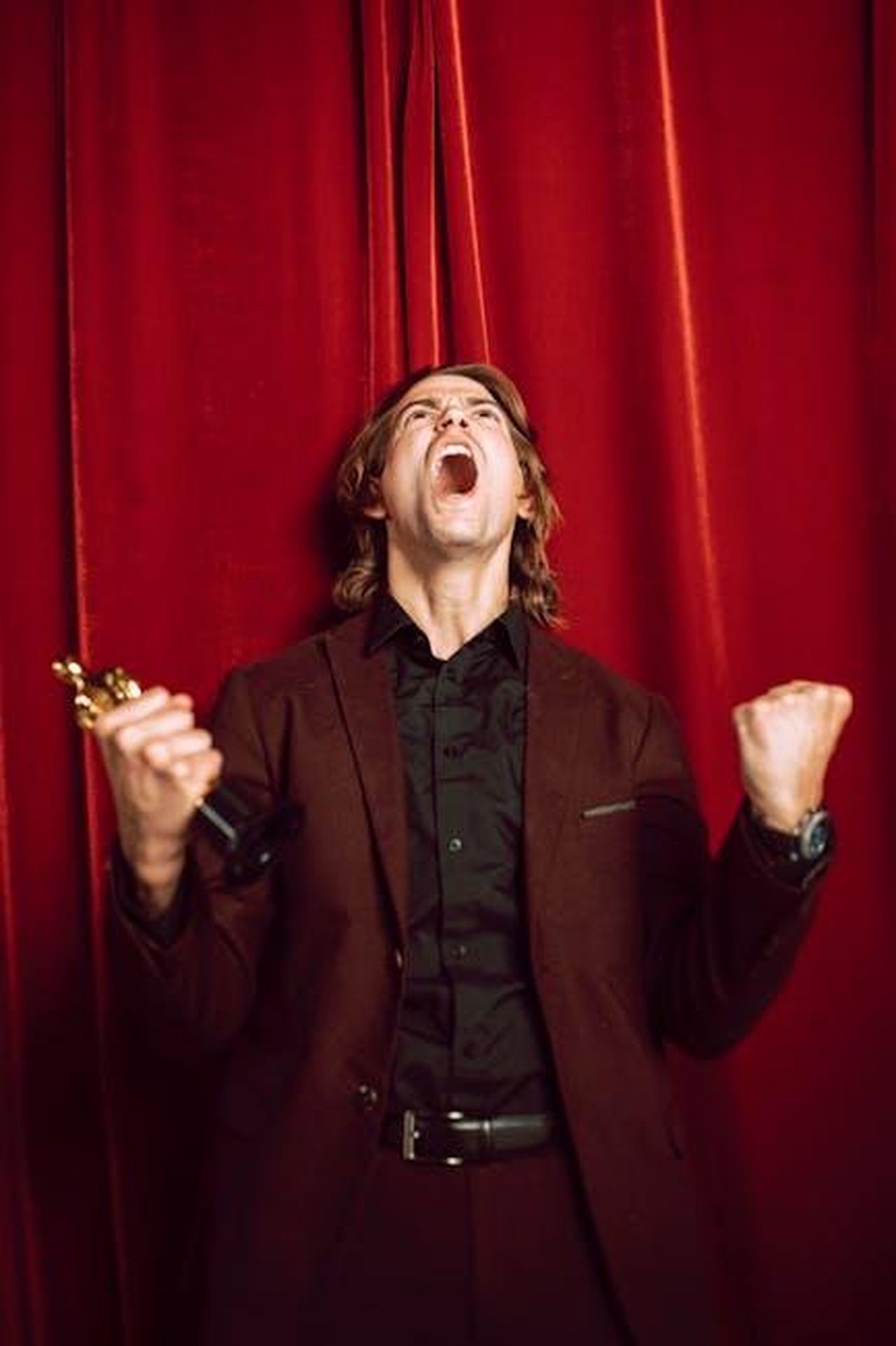 Tributi_e_performance_discutibili_DppM2GiibI - Confidenze24 Source: RDNE Stock project - pexels - Man in tuxedo celebrating with award trophy against a vibrant red curtain backdrop.
