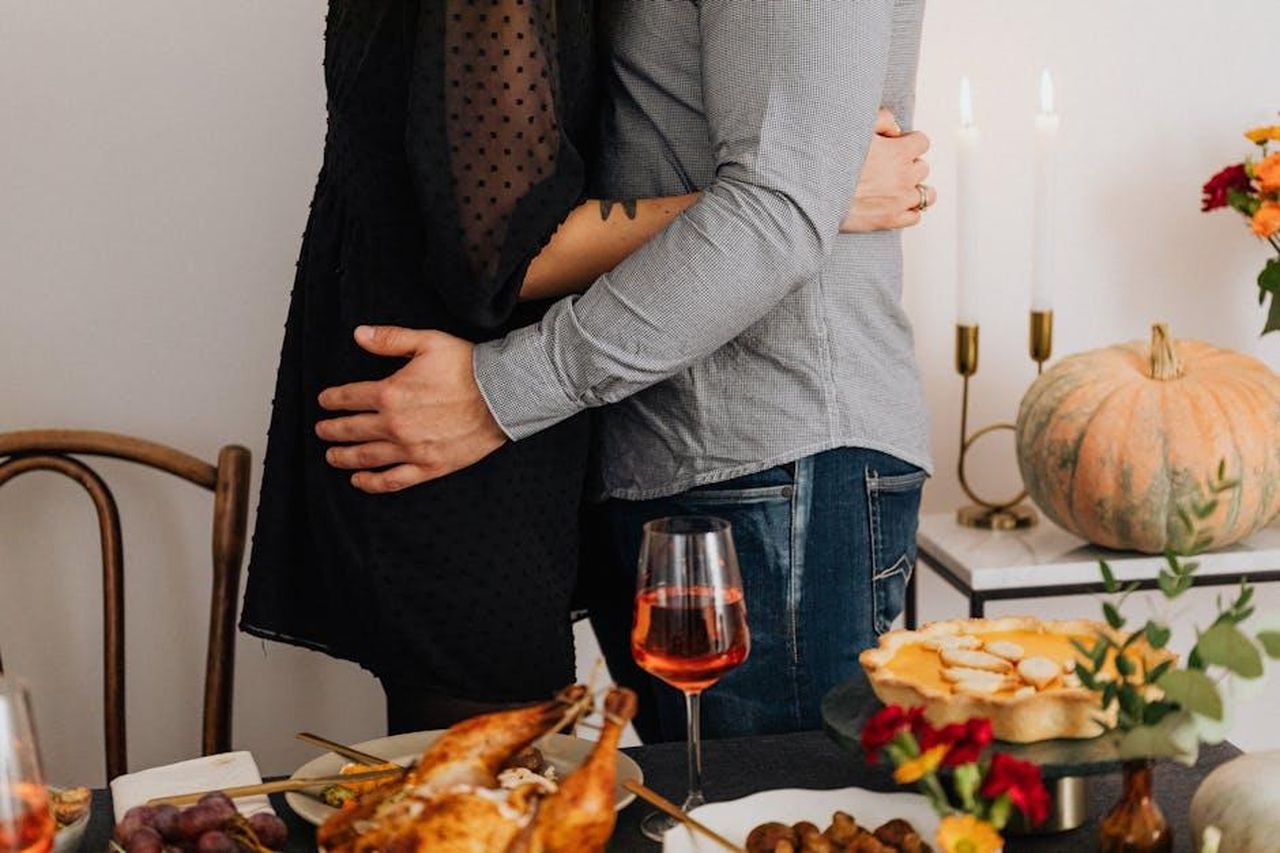 Un_Thanksgiving_del_passato_O7GTRGk2XD - Confidenze24 Source: Photo By: Kaboompics.com - pexels - Couple embracing amidst a Thanksgiving feast with turkey and wine.
