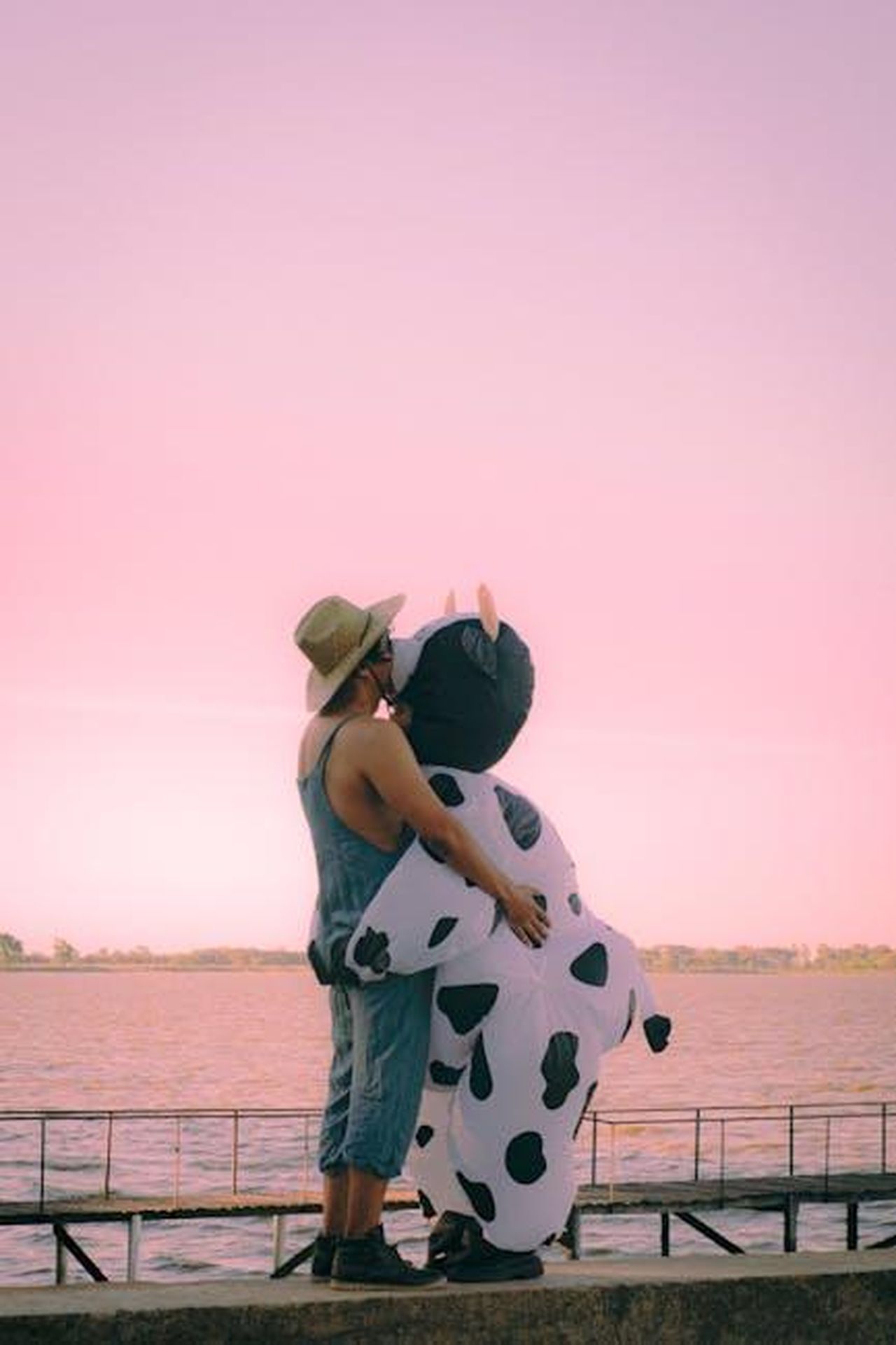 Un_amore_non_convenzionale_xey7FmcVcQ - Confidenze24 Source: Agustina Tolosa - pexels - A whimsical moment of affection with a person in a cow costume by the lakeside during sunset.