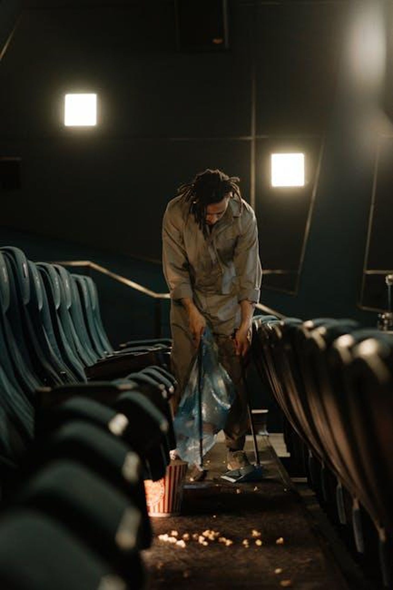 Un_film_non_avrebbe_senso_vEZjP3zuBb - Confidenze24 Source: cottonbro studio - pexels - A cinema staff member cleaning up popcorn in a dimly lit movie theater aisle.