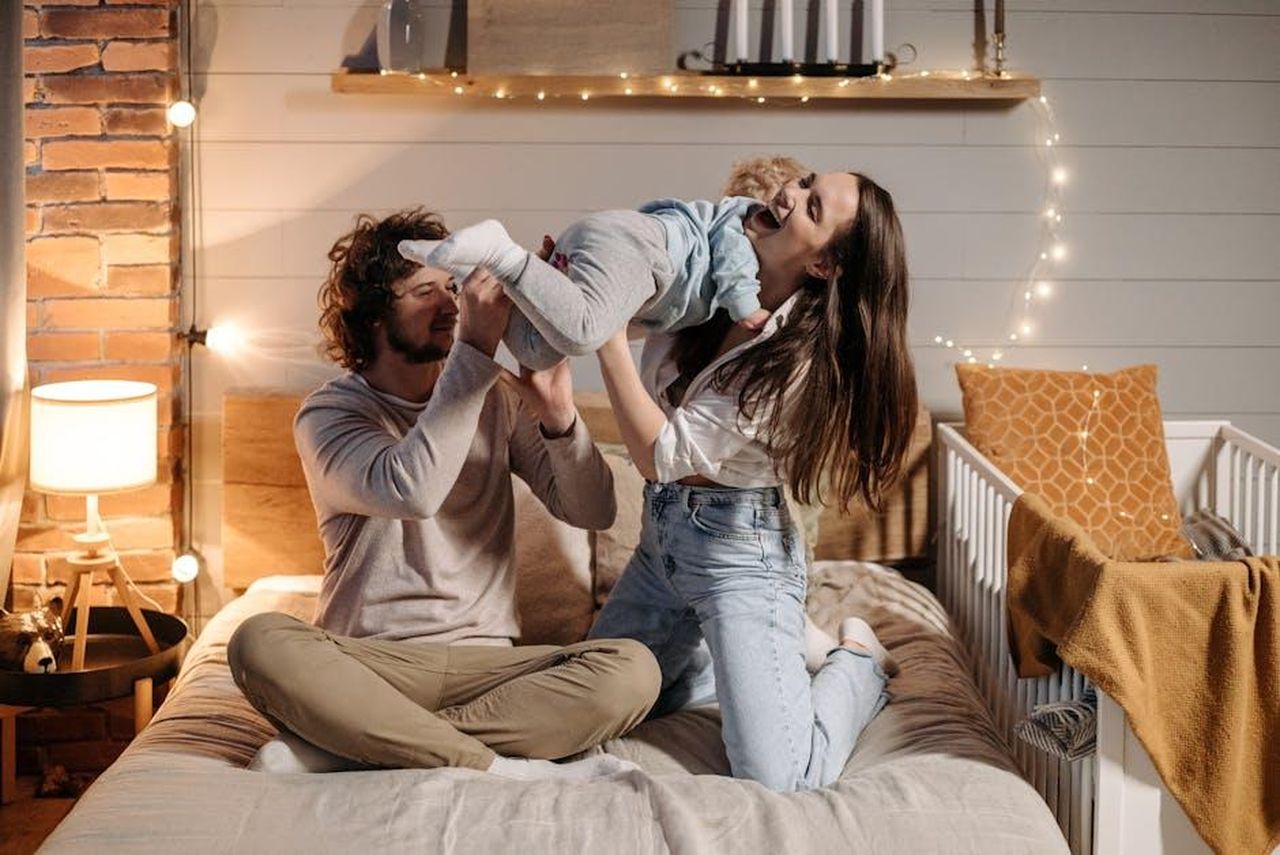 Un_momento_di_mamma_per_Paris_Hilton_LhlCjevwZf - Confidenze24 Source: Pavel Danilyuk - pexels - Joyful parents playing with their child on a bed in a warmly lit bedroom.