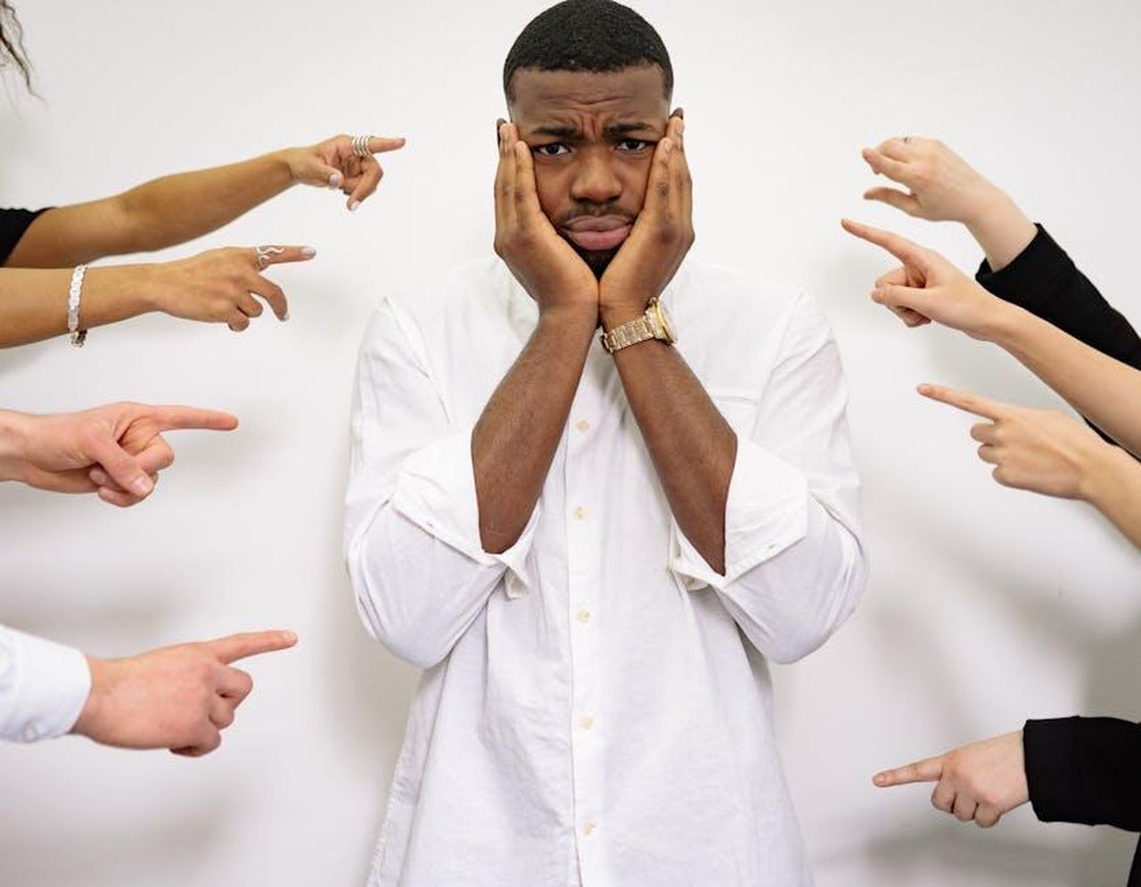 Un_momento_estremamente_difficile_A6mHS6gUCz - Confidenze24 Source: Yan Krukau - pexels - Worried man surrounded by pointing fingers, symbolizing bullying and social pressure.