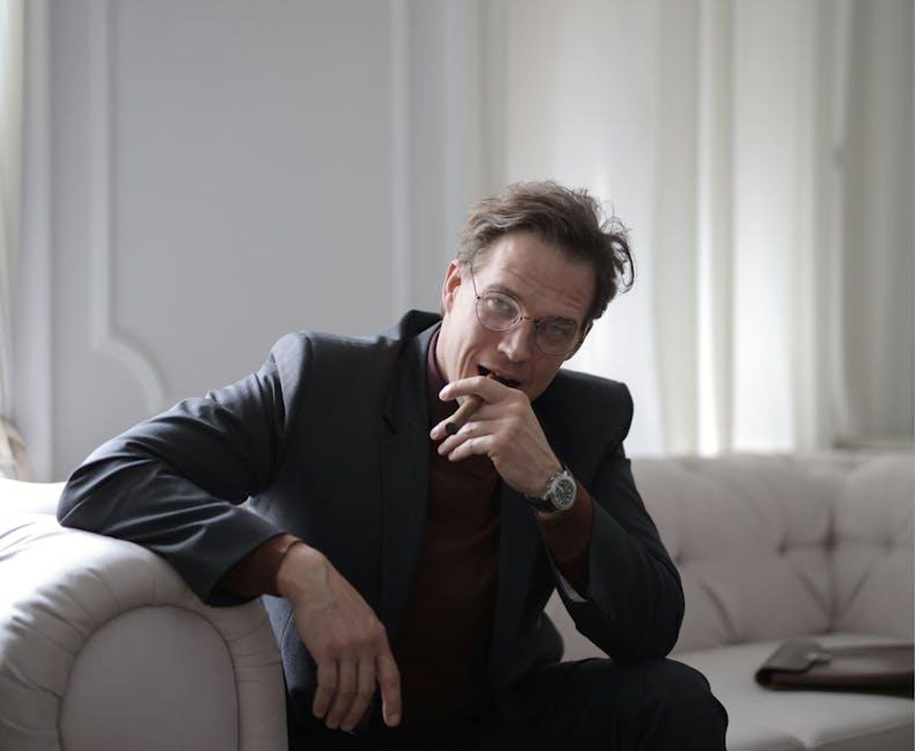Una_delle_cose_pi_difficili_che_ho_fatto_afFv1QYCQ2 - Confidenze24 Source: Andrea Piacquadio - pexels - A confident businessman in a black suit sitting on a sofa indoors with a thoughtful expression.