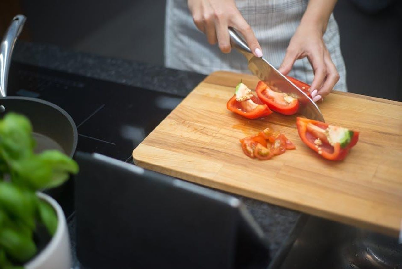 Unalternativa_economica_a_Le_Creuset_oI6GRMRRU3 - Confidenze24 Source: Kampus Production - pexels - Close-up of a woman slicing red bell pepper in a modern kitchen setting.