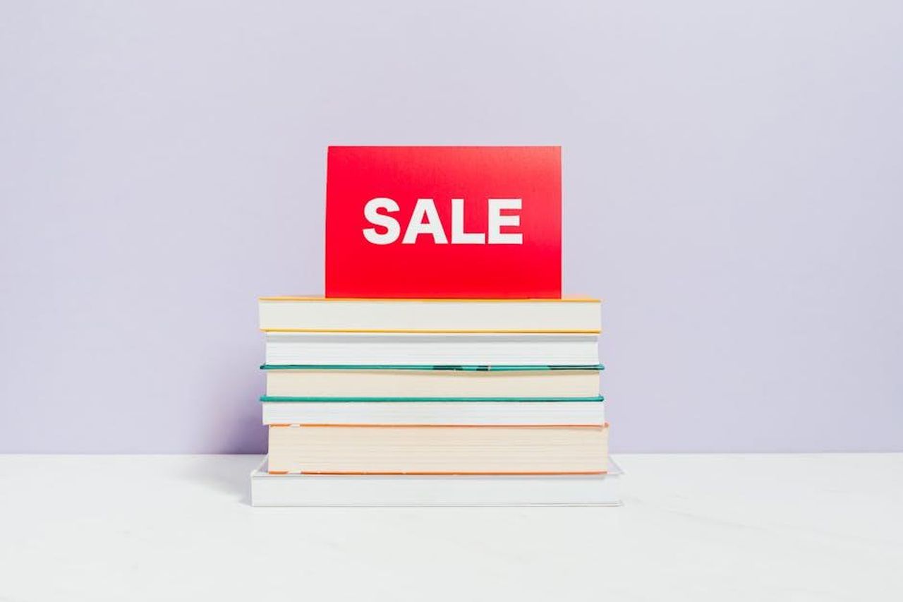 Unalternativa_economica_ai_plumper_tradizionali_a53jfAOgoO - Confidenze24 Source: Photo By: Kaboompics.com - pexels - A stack of books with a red sale sign, ideal for promotions and bookshop advertisements.