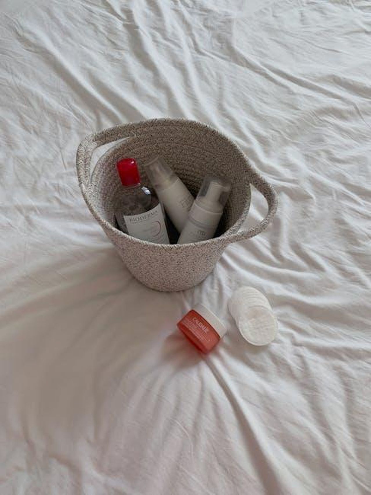 Unopzione_economica_per_tutti_FGwg8GpMww - Confidenze24 Source: Inna Gritsenko - pexels - A collection of skincare products elegantly arranged in a woven basket on white bed sheets.