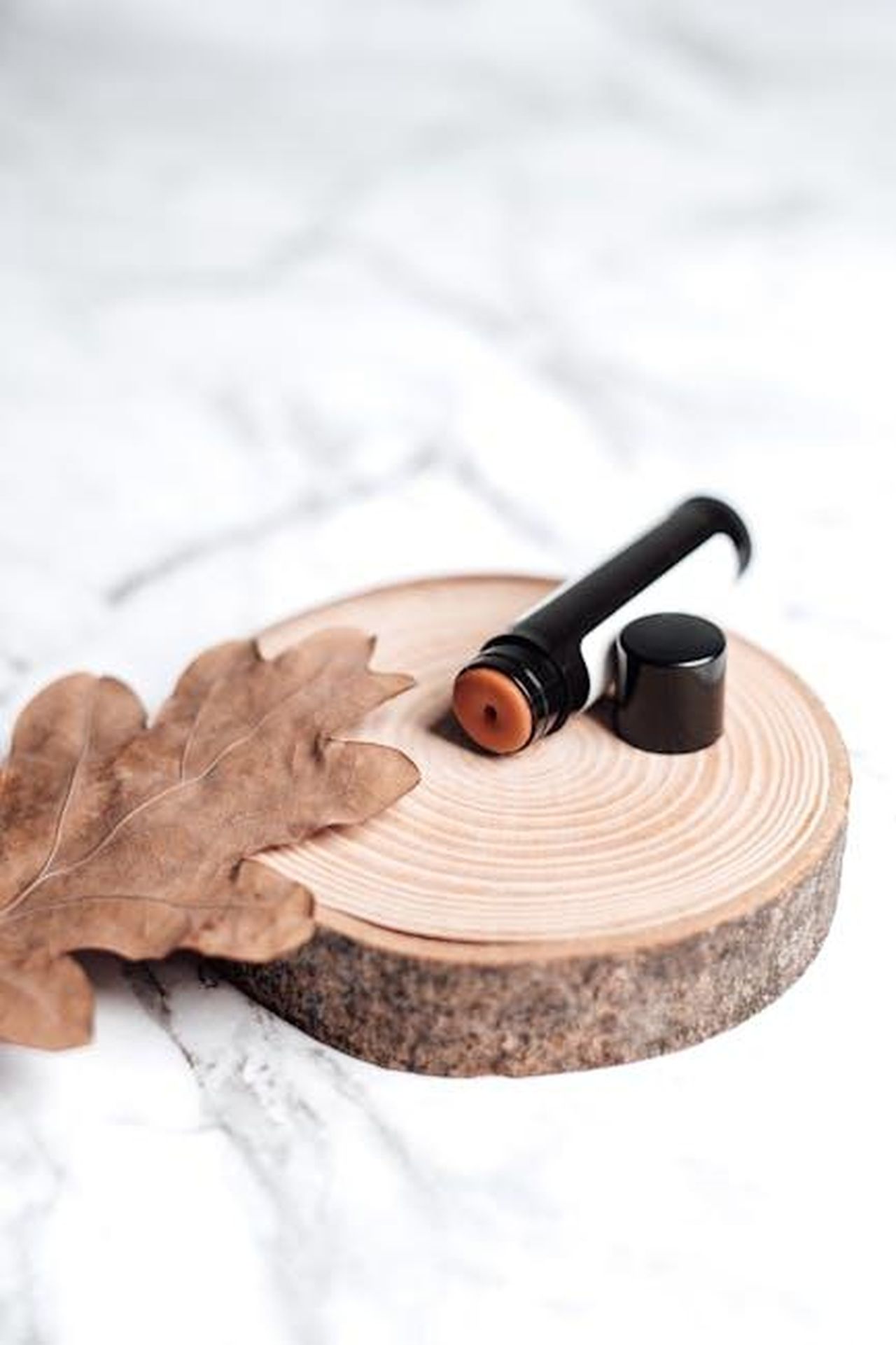 Vantaggi_del_formato_stick_del_prodotto_6rOxAau8c8 - Confidenze24 Source: Vie Studio - pexels - Close-up of lip balm on a wooden slice against a marble background, featuring a dried leaf.