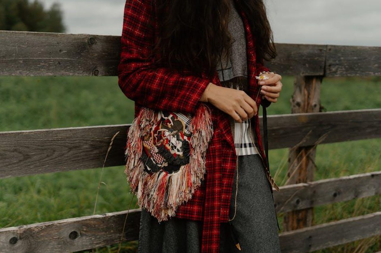Vergine_23_AGOSTO__22_SETTEMBRE_tZVLClrwlr - Confidenze24 Source: cottonbro studio - pexels - A woman in boho attire with an embroidered bag leaning on a wooden fence outdoors.