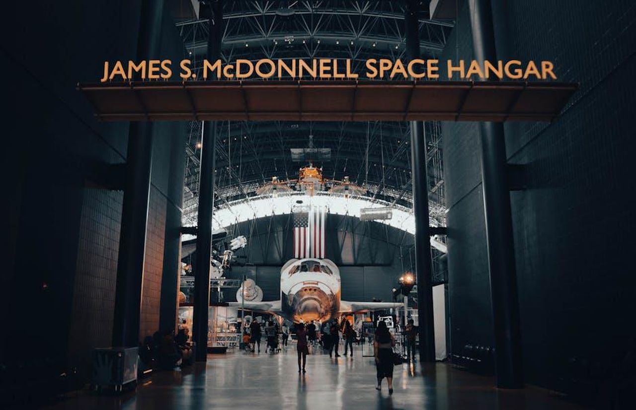 Visite_della_famiglia_di_Meghan_sul_set_iZalT1Ytrz - Confidenze24 Source: Eleanore Stohner - pexels - Interior view of the James S. McDonnell Space Hangar featuring a showcased spacecraft with visitors exploring.