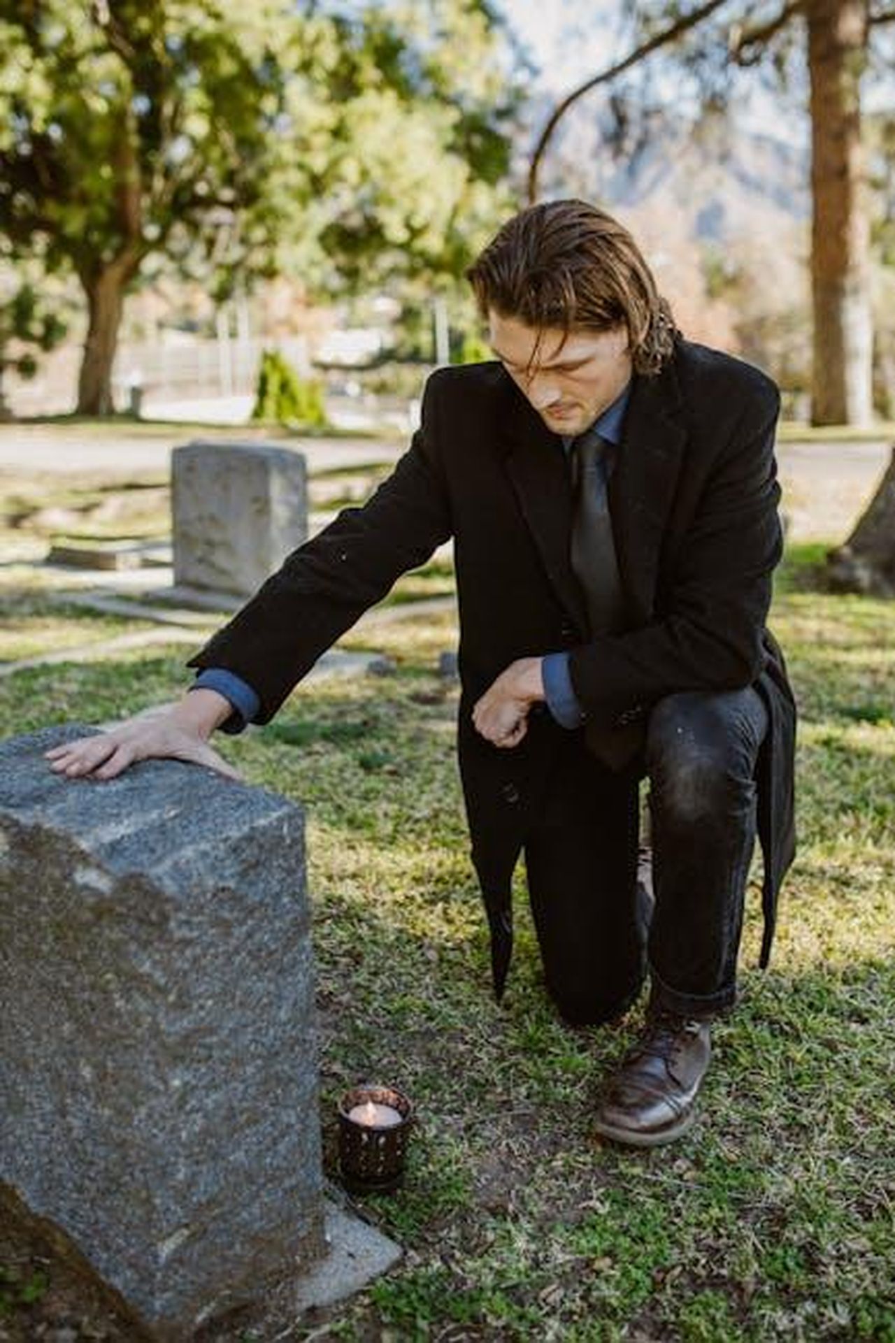 Vivere_la_Vita_Secondo_le_Sue_Regole_Dopo_la_Morte_del_Padre_q3FxGsMQ0y - Confidenze24 Source: RDNE Stock project - pexels - A man kneels by a gravestone in a sunny cemetery, reflecting on loss and healing.
