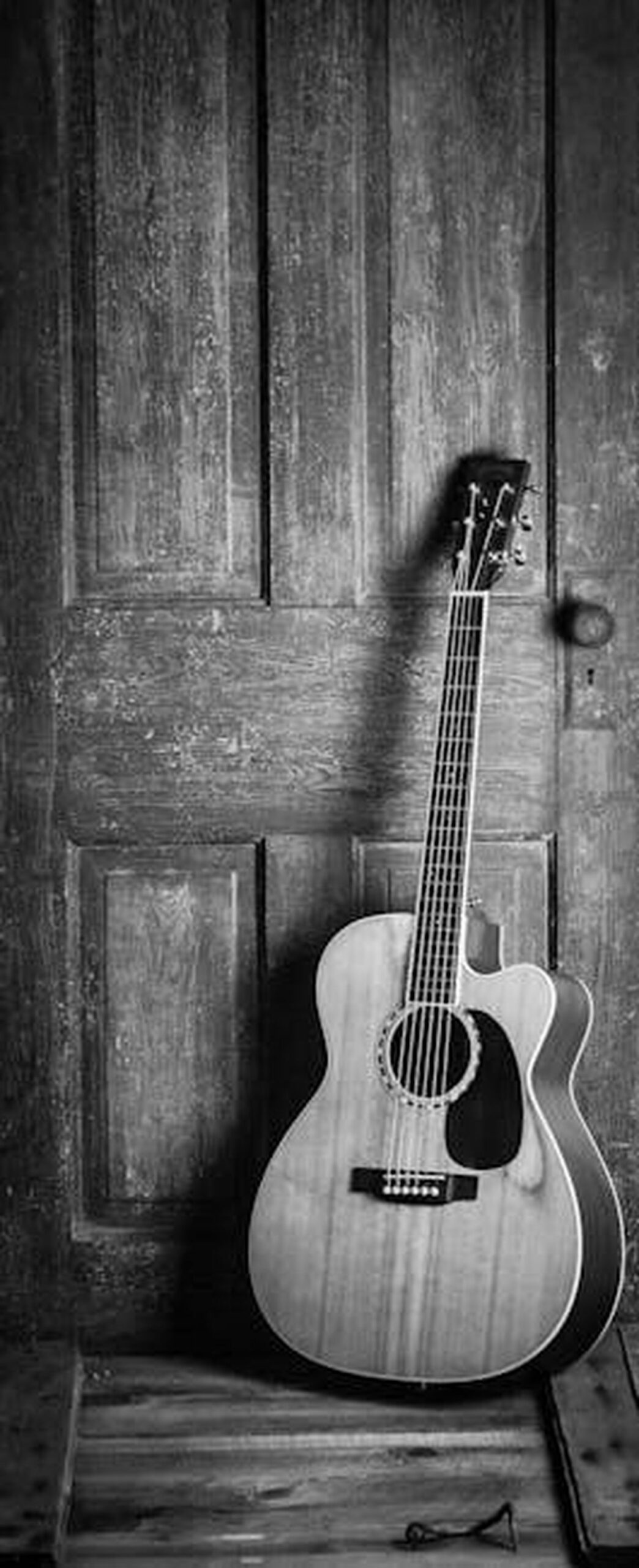 Will_Smith_fa_un_ritorno_musicale_YEvTVVpAJ3 - Confidenze24 Source: Jessica Lewis 🦋 thepaintedsquare - pexels - A classic acoustic guitar leaning against a rustic wooden door in a black and white vintage style.
