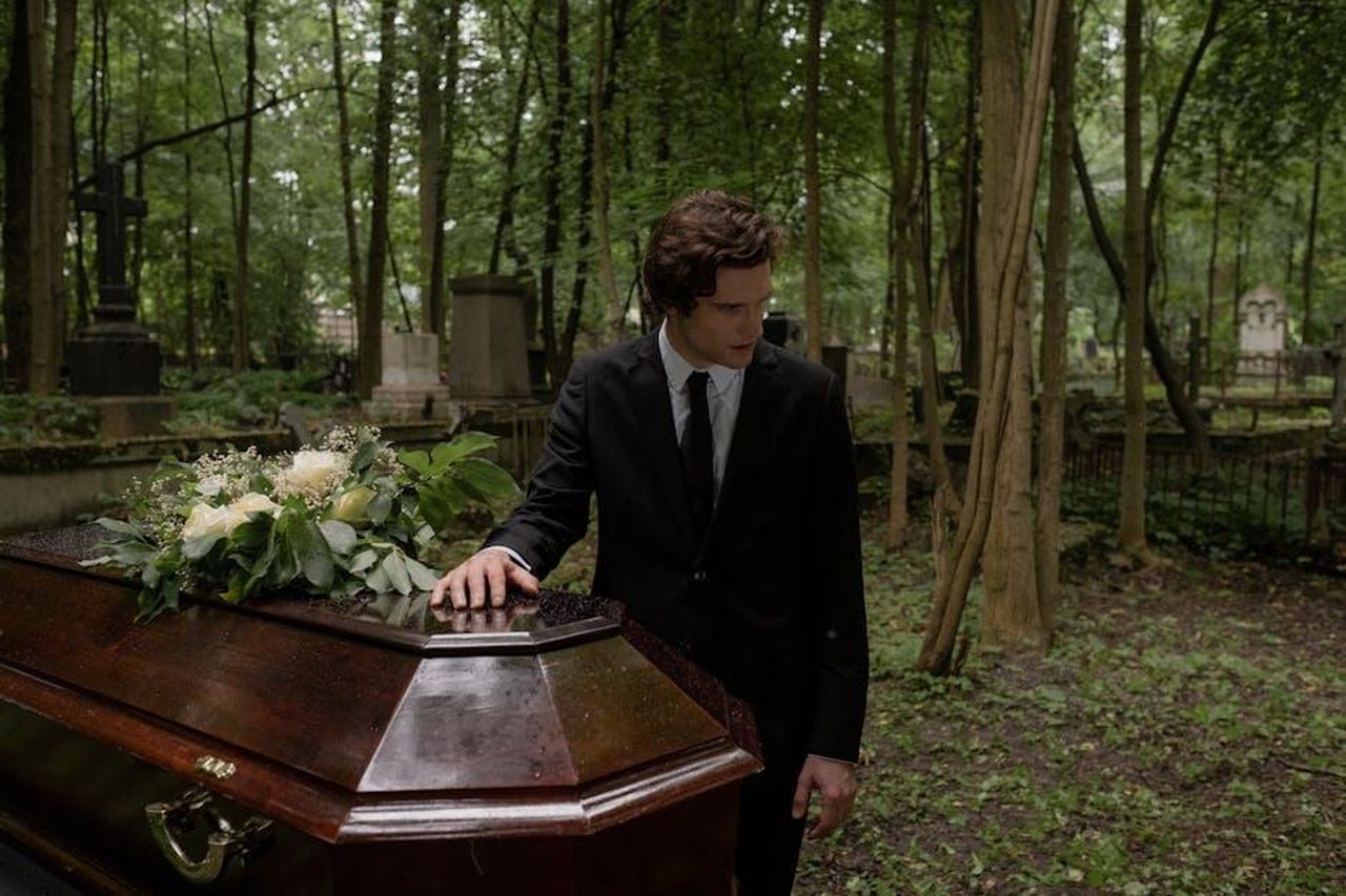 Yasmeen_ha_lasciato_Coronation_Street_per_sempre_6bM91S5g3i - Confidenze24 Source: cottonbro studio - pexels - A man in a black suit mourns at a funeral in a lush green cemetery, leaning on the coffin.
