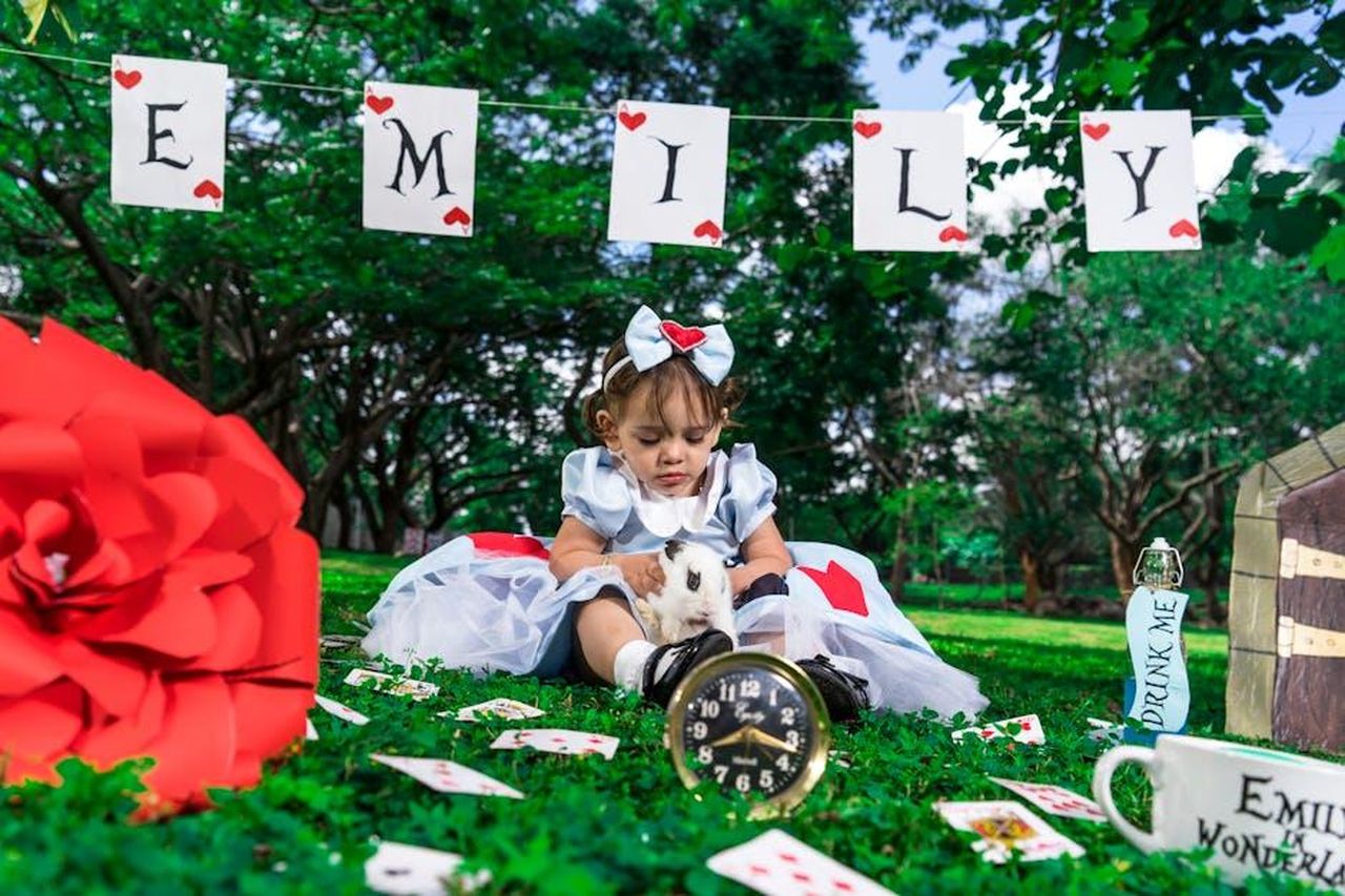 _madre_di_due_bambini_tEeNpOlUD4 - Confidenze24 Source: Becerra Govea Photo - pexels - A child in Alice costume sits with a rabbit in a whimsical garden setting, surrounded by themed decorations.