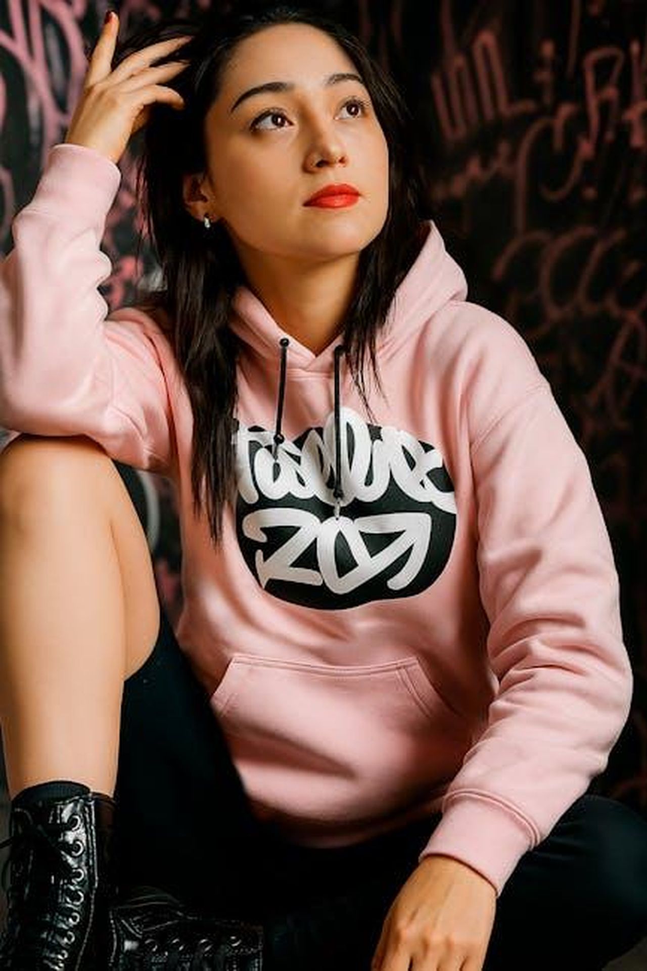 Cat_risponde_alle_critiche_BOf8dFTAb1 - Confidenze24 Source: Rodrigo Morelos Oseguera - pexels - Young woman in a pink hoodie posing against graffiti wall. Urban fashion shot capturing contemporary style.