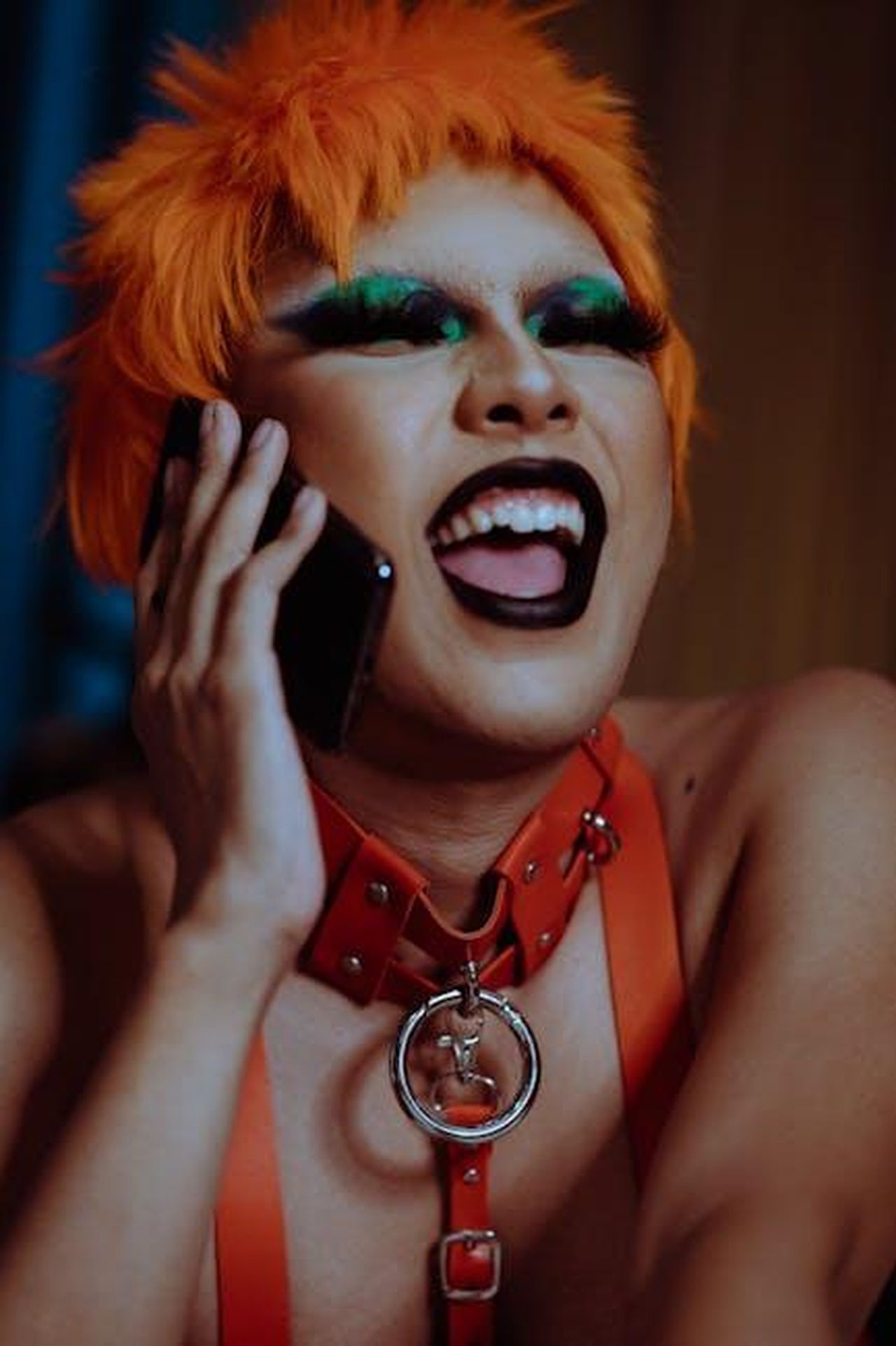 Conversazioni_su_chi_deve_sapere_RlzZ4rjfeA - Confidenze24 Source: Kamaji Ogino - pexels - A young person with bold makeup and orange hair in vibrant fashion, talking on a phone.