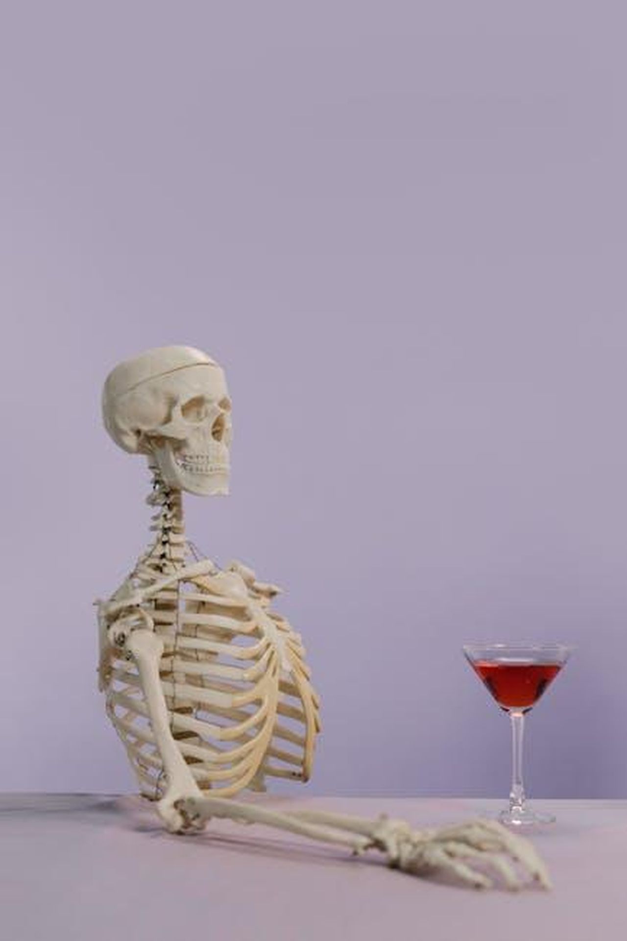Denise_si__unita_alla_storia_qyvoctk3yB - Confidenze24 Source: cottonbro studio - pexels - Skeleton model with a cocktail glass on a purple background, playful and intriguing vibe.
