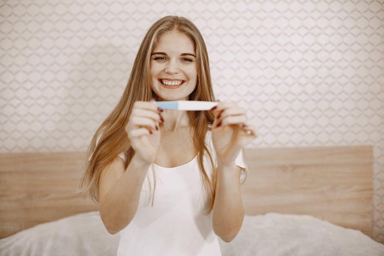 Dianne_Buswell_e_Joe_Sugg_accennano_a_piani_per_un_bambino_F9exRy2dDr - Confidenze24 Source: Gustavo Fring - pexels - Excited woman happily displaying her positive pregnancy test in a cozy bedroom setting.