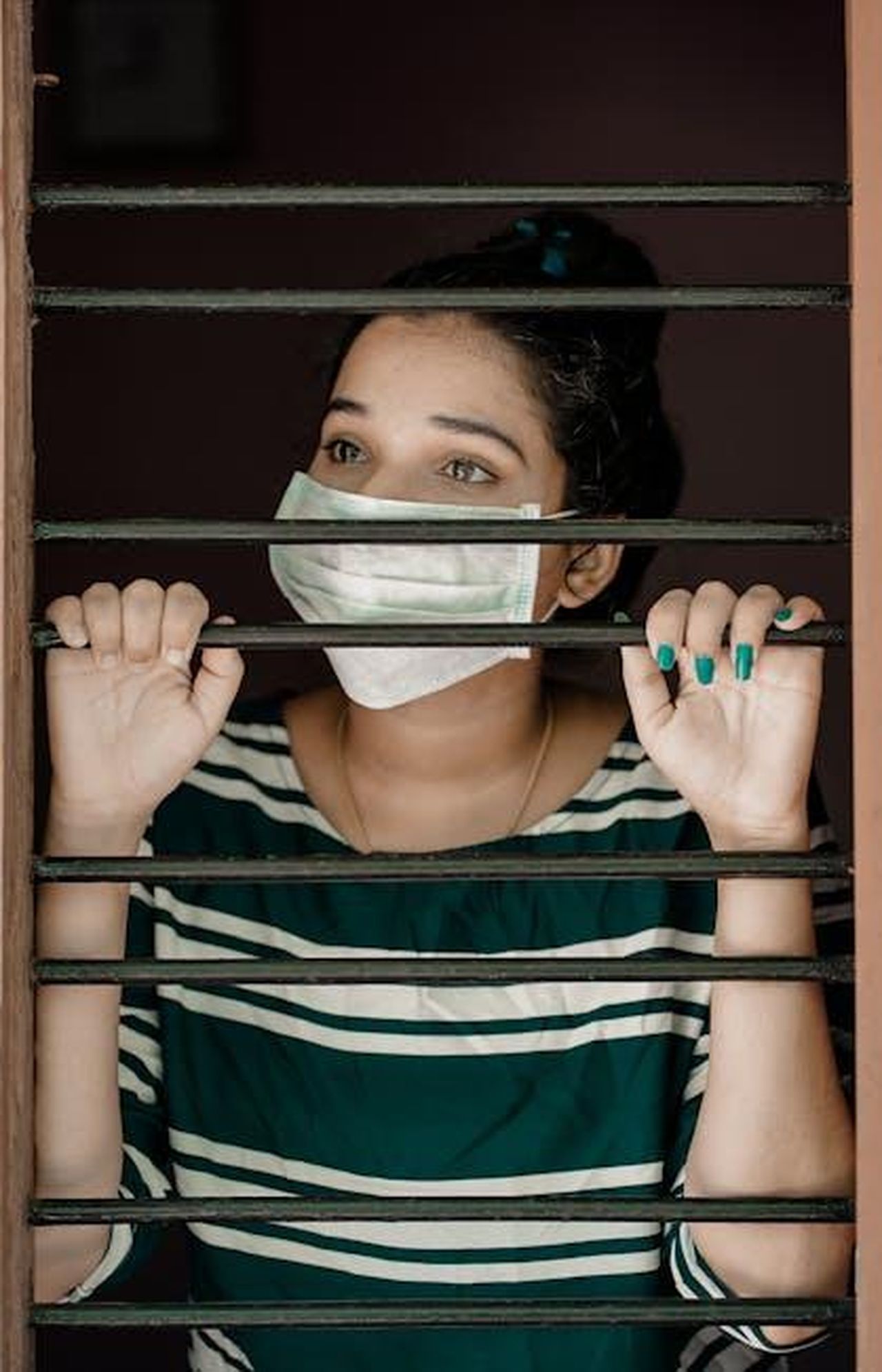 Harry_e_la_sua_solitudine_a_Montecito_FvzPauM8cj - Confidenze24 Source: Nandhu Kumar - pexels - A woman wearing a face mask looks through window bars during COVID-19 lockdown.