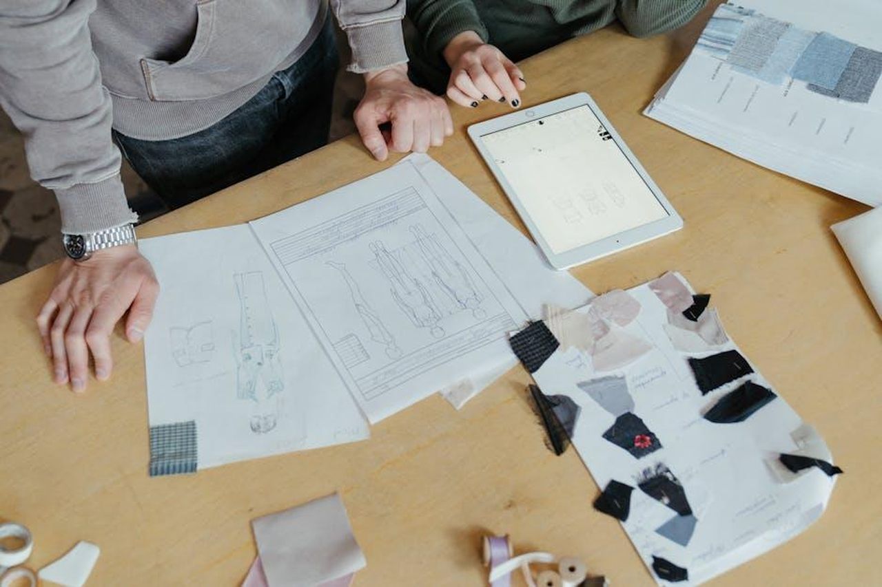 Il_designer_Myah_Hasbany_e_la_sua_collaborazione_con_Badu_OuePRMiWBR - Confidenze24 Source: cottonbro studio - pexels - Two designers examine clothing sketches and fabric swatches on a worktable, highlighting fashion creativity.