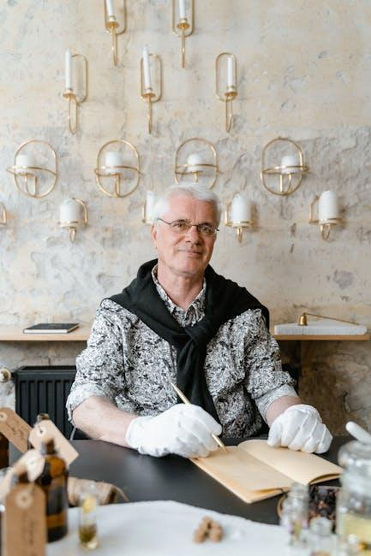 Il_nuovo_memoir_di_Fiona_seeyJHmcZR - Confidenze24 Source: MART PRODUCTION - pexels - A senior man wearing gloves writes in a notebook surrounded by elegant decor.