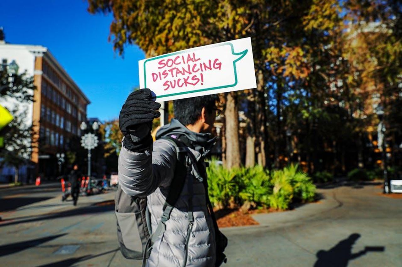 La_reazione_del_pubblico_Bc26iSnDpK - Confidenze24 Source: Mick Haupt - pexels - Person outdoors in Orlando holding a sign saying 'Social Distancing Sucks!'.