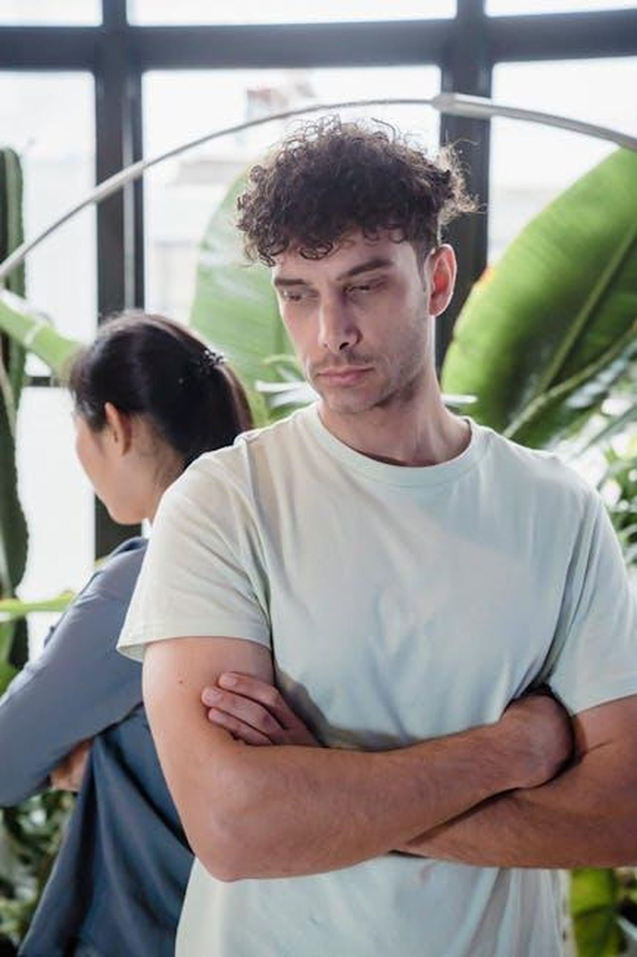 La_relazione_di_Tom_e_Charlotte_alti_e_bassi_7HKVmqT0sH - Confidenze24 Source: Timur Weber - pexels - A couple standing back to back amidst indoor plants, expressing misunderstanding.
