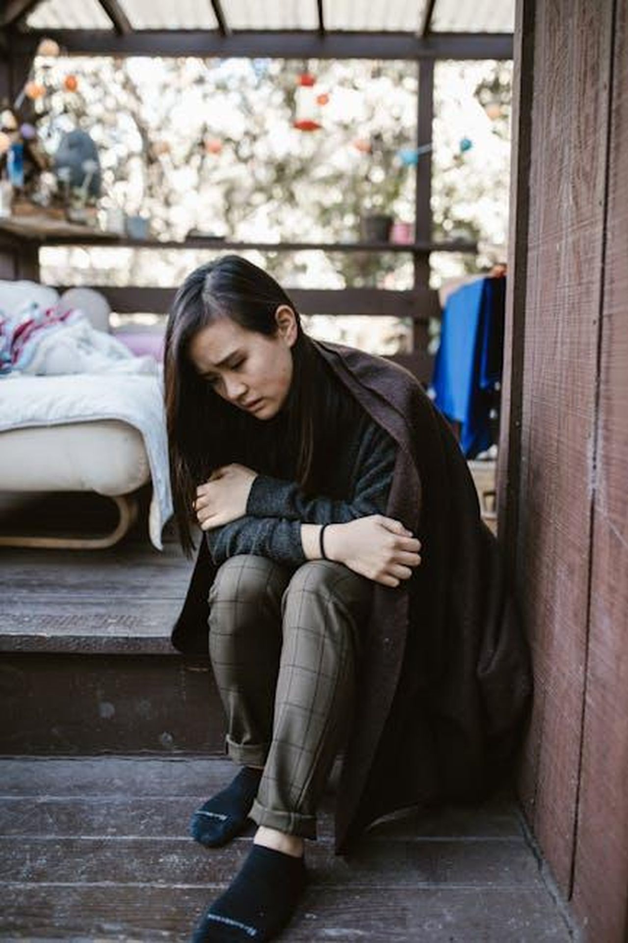 La_solitudine_di_Harry_in_California_H20iRrkSjc - Confidenze24 Source: RDNE Stock project - pexels - A woman sits alone, deep in thought on a wooden deck with a cozy background.