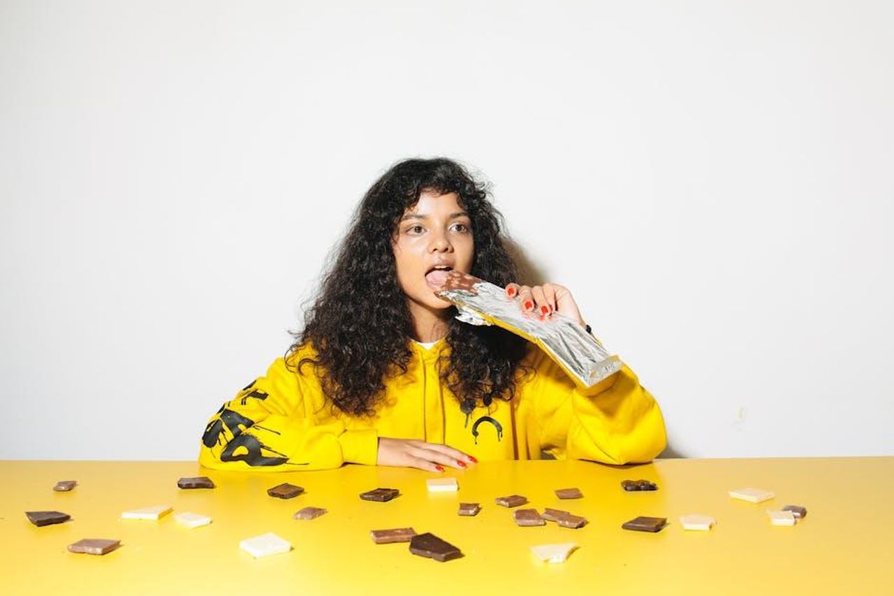 La_variet_di_contenuti_su_YouTube_YZ5sZEDilZ - Confidenze24 Source: Polina Tankilevitch - pexels - A young woman in a yellow hoodie enjoying chocolate pieces at a table. Bright scene.
