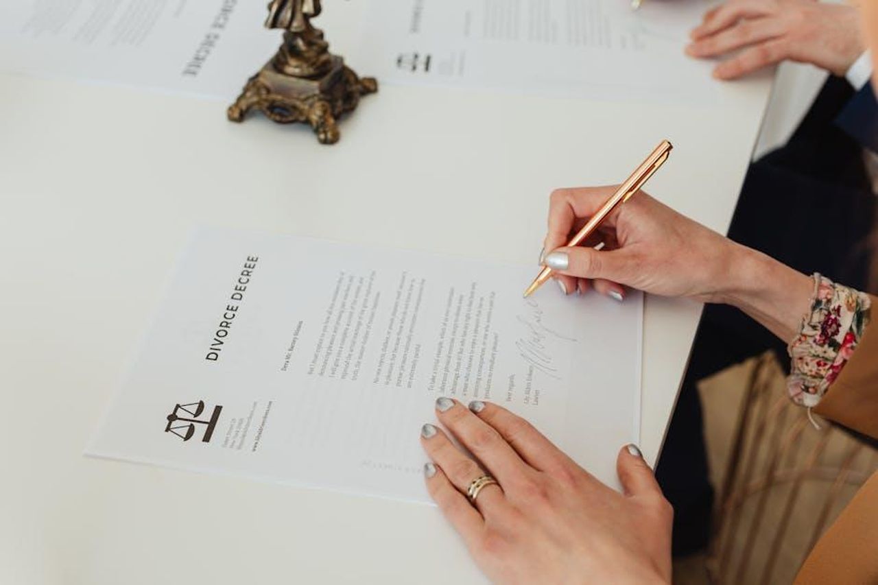 Le_accuse_di_Ashley_St_Clair_contro_Elon_Musk_LjUMJ58BZm - Confidenze24 Source: Photo By: Kaboompics.com - pexels - Close-up of hands signing a divorce decree document on a desk, showcasing legal process.