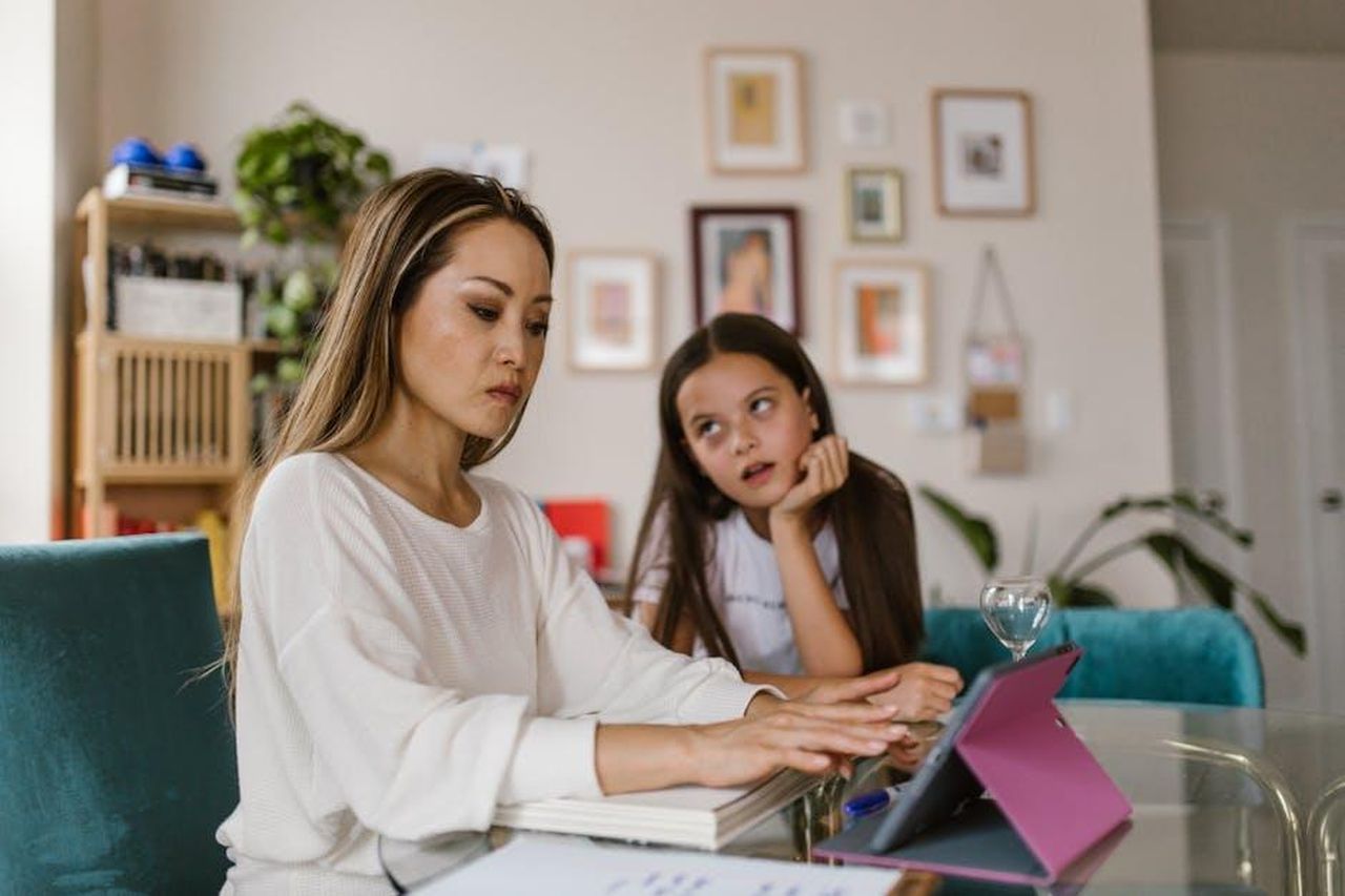 Le_sfide_della_maternit_secondo_Chappell_Roan_SY9VJ8Hooz - Confidenze24 Source: RDNE Stock project - pexels - A mother working on her tablet at home while her daughter watches from nearby, illustrating remote work challenges.