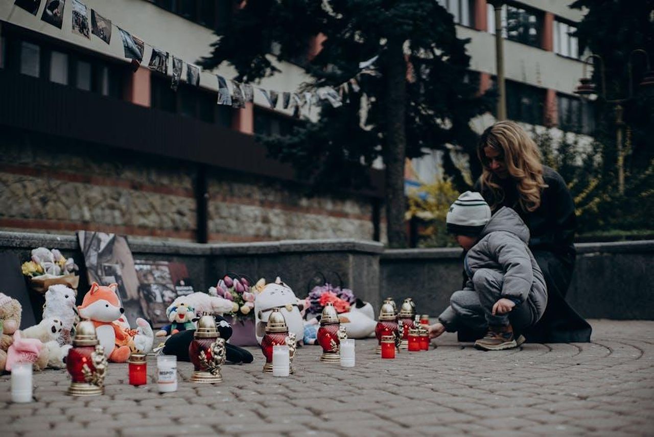 Lultimo_attacco_di_Jeff_a_Jackiey_Zo7UxQ1L0c - Confidenze24 Source: Антон Залевський - pexels - Mother and child paying tribute with candles and gifts at a memorial in Ukraine, showcasing remembrance and emotional connection.