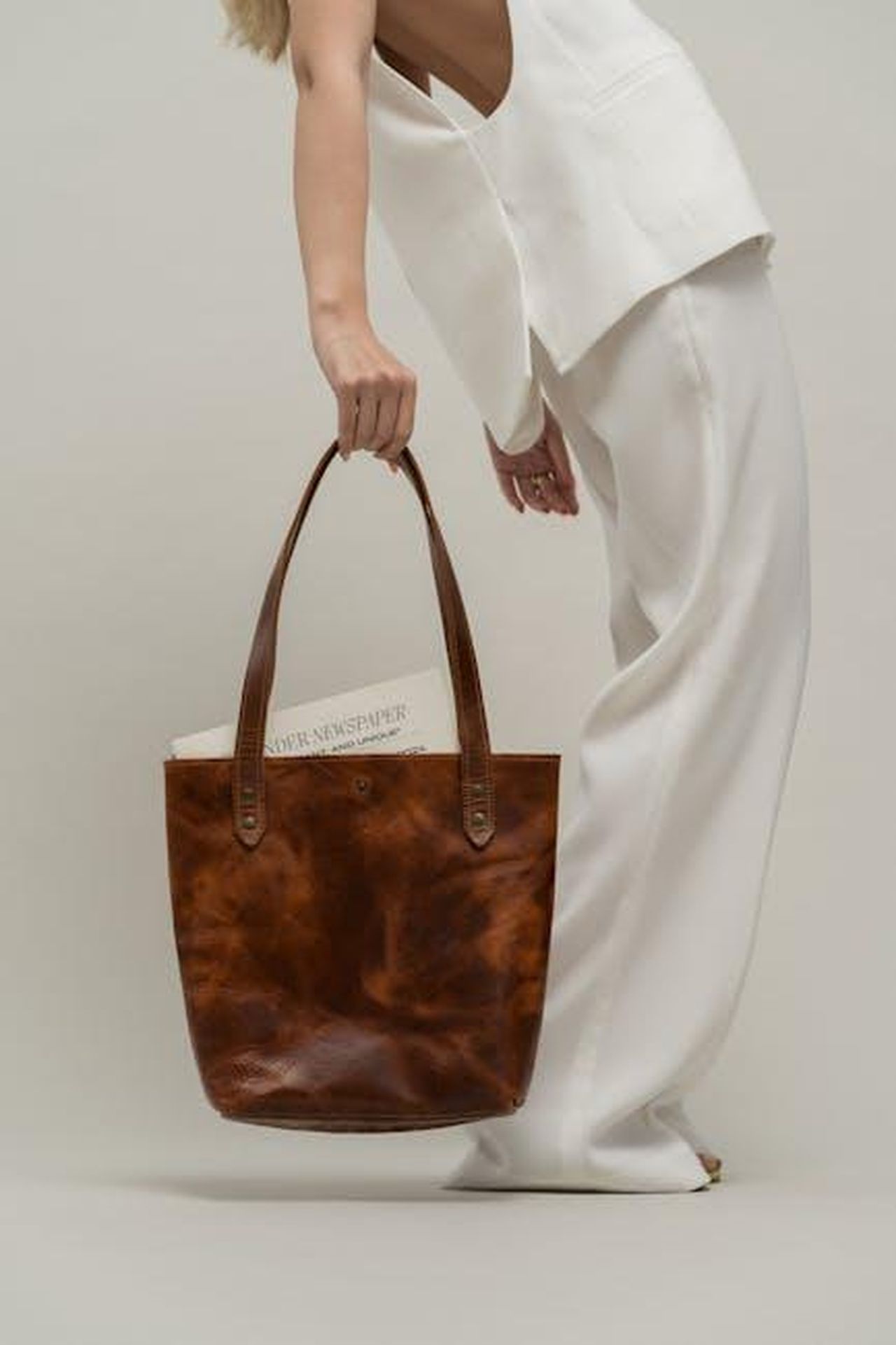 Mini_Ella_Bio_Tote_EcoFriendly_e_Chic_TXheFl3dFP - Confidenze24 Source: Gül Işık - pexels - Stylish woman holding a brown leather bag in a minimalist studio setting.