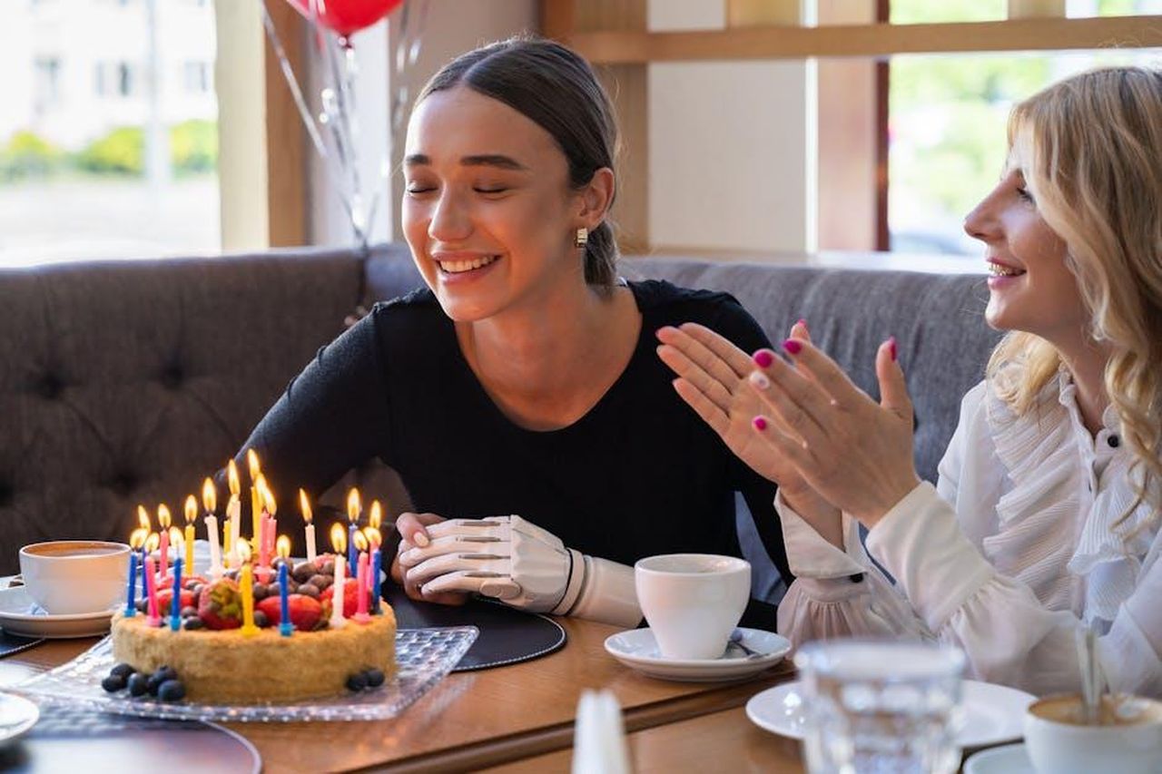 Paul_Hollywood_sostiene_la_vittoria_di_Kate_us9iKeDl46 - Confidenze24 Source: Mikhail Nilov - pexels - Happy birthday celebration with friends, cake, and prosthetic arm in cozy café setting.