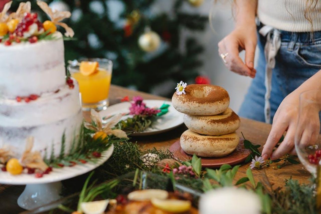 Preparazione_dei_bagel_alla_cannella_UY7KI5ExMk - Confidenze24 Source: Tim Douglas - pexels - A festive table with a layered cake, bagels, flowers, and holiday decor. Perfect for Christmas celebrations.