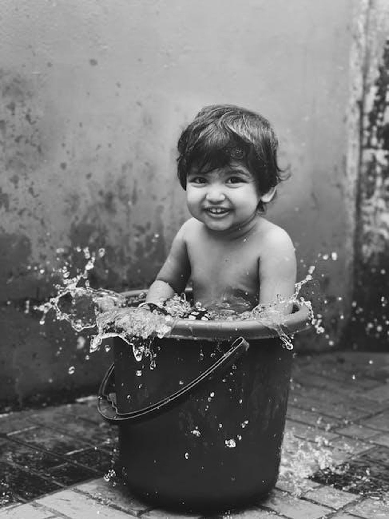 Rendere_il_bagno_divertente_DaR1EdrZUg - Confidenze24 Source: Ajinas P.K - pexels - Cute child enjoying a splash in a bucket, embodying pure joy and innocence outdoors.