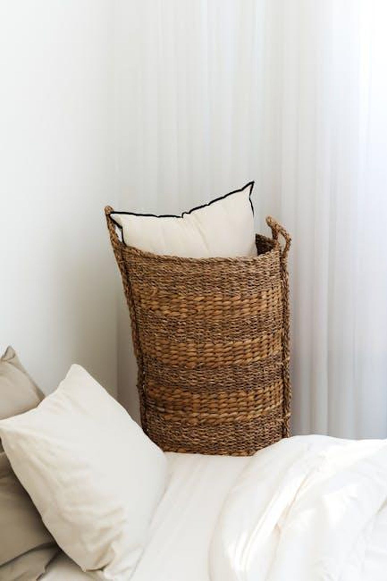 Sir_Michael_Fabricant_firma_per_un_contratto_da_sei_cifre_REfOk3T2kd - Confidenze24 Source: Kader D. Kahraman - pexels - Minimalist bedroom featuring a wicker basket with pillows and neutral bedding.