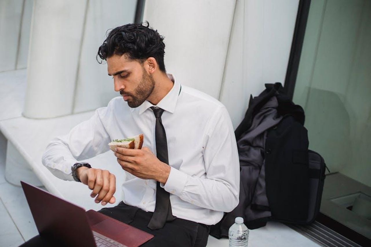 Trucchi_per_far_mangiare_i_bambini_Ov3bdHyZKA - Confidenze24 Source: Ketut Subiyanto - pexels - Businessman in formal attire eating a sandwich while checking his watch outdoors, multitasking during break.